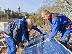 Drei Männer montieren auf Dach eine Photovoltaik-Anlage.
